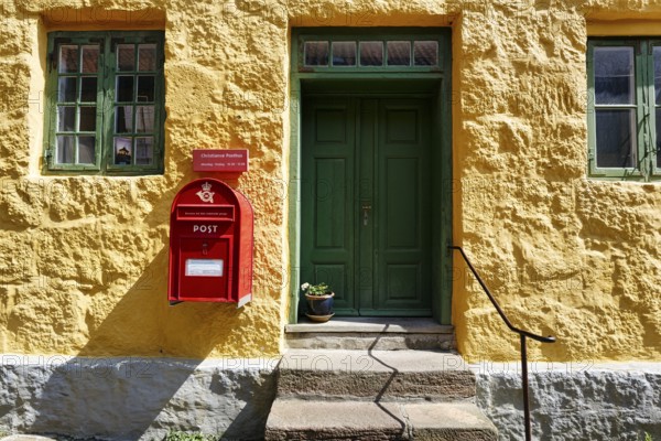 Post office, faÃ§ade detail, red mailbox with post horn and crown, green wooden door, yellow wall,