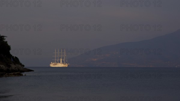A large sailing ship sails in the calm sea in front of a dark mountain silhouette, Nauplion,