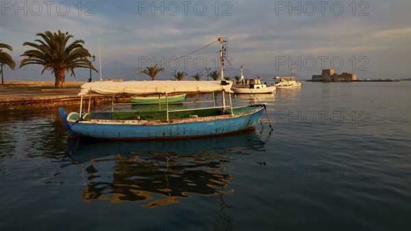Port of Nauplion, Bourtzi island fortress, A blue boat in the harbor with palm trees and view of a