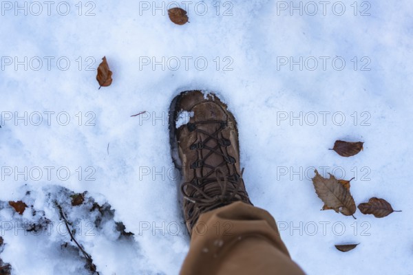 Hiker's brown boot and light pants stepping through fresh white snow scattered with dry brown