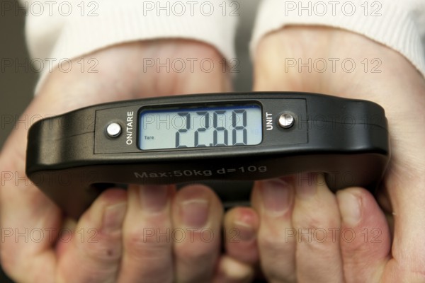 Woman holding hand scale for weight of suitcase travel bag flight luggage checks luggage weight for