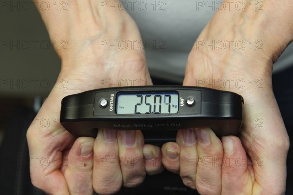 Woman holding hand scale for weight of suitcase travel bag flight luggage checks luggage weight for