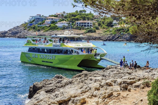 Tourists get on board a glass-bottom boat docks at the small bay Font de Sa Cala on the east coast