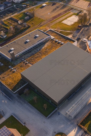Sports center and swimming pool with flat roof and adjacent parking lot, surrounded by green areas