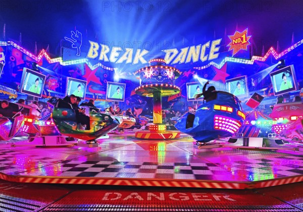 People in the colorful illuminated break dance ride at night at the All Saints Fair, Soest, North