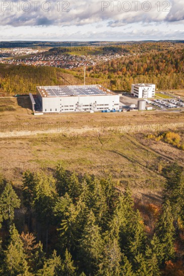 Factory building next to forest and clearing, behind a village on a hill in autumn tones, new