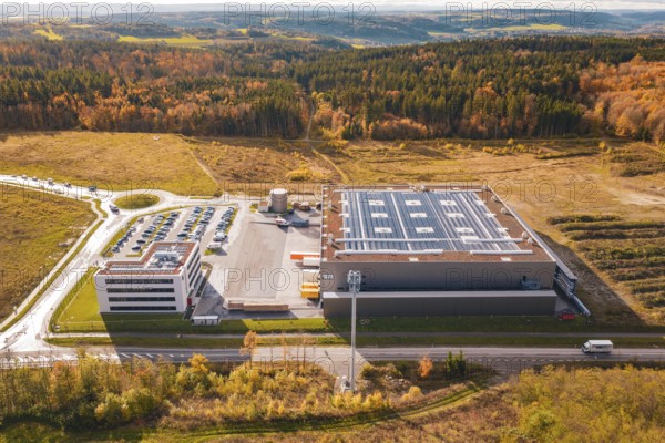 Large factory with parking lot, surrounded by forest and open spaces in an autumnal setting, new