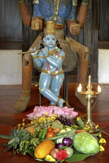 Sculpture of shepherd god Krishna playing his flute, fruits and vegetables lying on the ground,