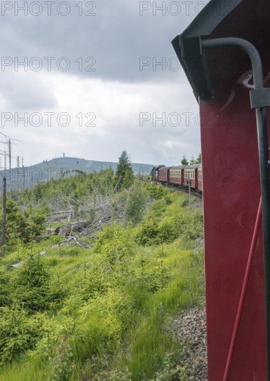 The locomotive of the historic Brocken Railway with several red and white wagons travels from Drei