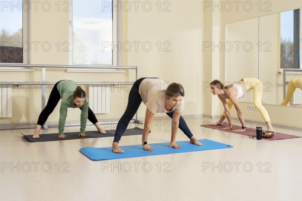 In a spacious yoga studio, three women are engaged in a group class. They are performing various