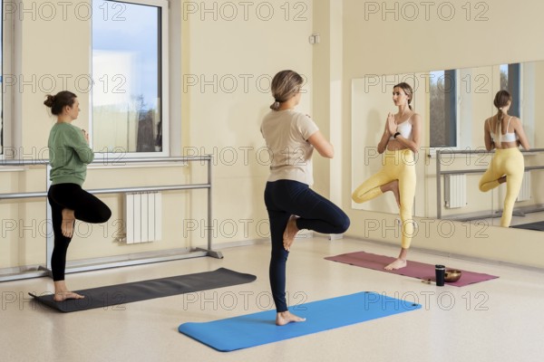Three women practice yoga in a well-lit studio, showcasing various poses that emphasize balance. A