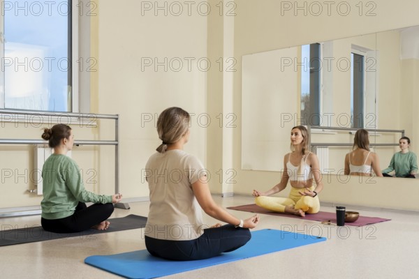 Three individuals practice meditation in a well-lit studio, focusing on relaxation. Soft mats are