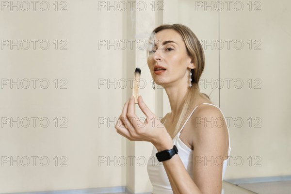 A woman with long hair is sitting calmly and gently holding an incense stick. Smoke is rising