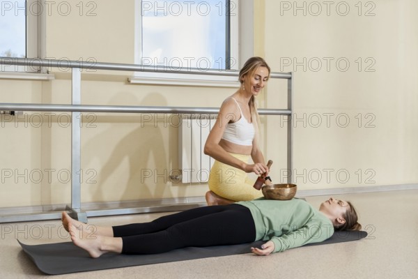 An instructor uses a singing bowl to provide sound therapy to a relaxed participant lying on a mat