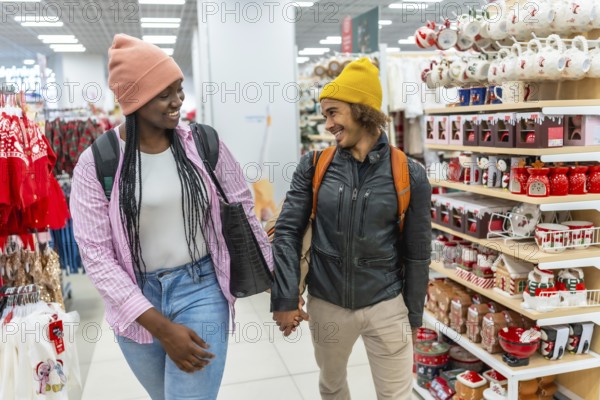 Diverse young couple smiling while holding hands, shopping together in a store, browsing shelves