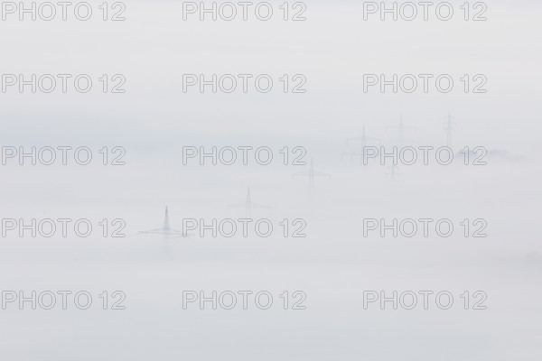 High-voltage pylons rise up from the thick sea of fog, silence and technology the silhouette of