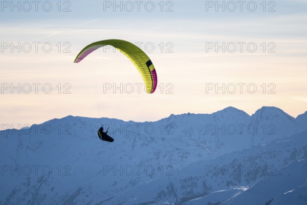 Paragliders flying over snowy mountain peaks in winter in evening light, KitzbÃ¼hel Alps, Tyrol,
