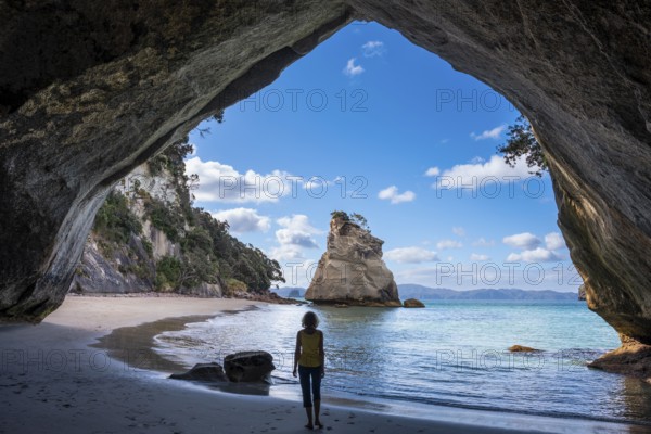 A woman in Cathedral Cove in New Zealand. Sea, sandy beach and limestone cliffs. The cave itself