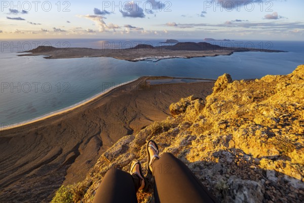First person view, legs of a woman sitting on a steep cliff, view of the sea and the island of La