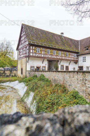 Well-preserved traditional half-timbered house next to a stone wall in a rural area, Wasserschloss