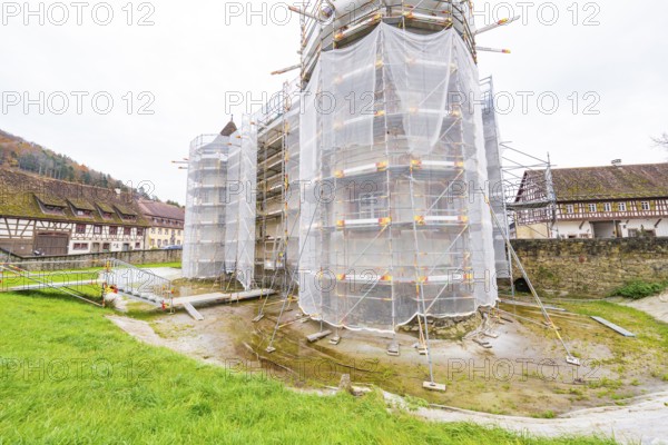 A rural-style renovated building with scaffolding and tarpaulins, surrounded by green spaces,