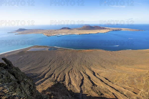 View of steep cliffs by the sea and island of La Graciosa with volcanic craters in the evening