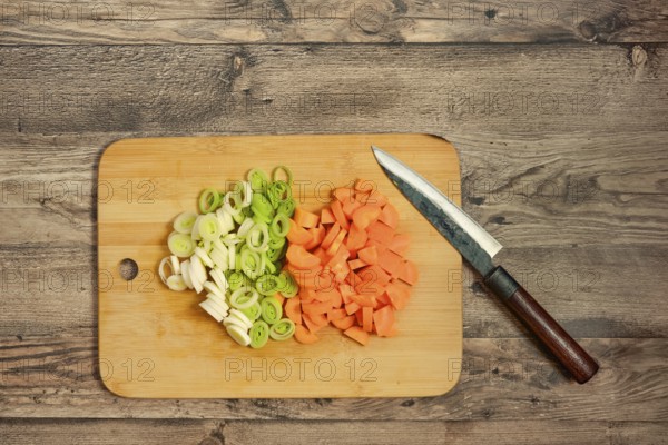 Fresh leek onion and carrots are chopped and neatly arranged on a wooden cutting board. A sharp