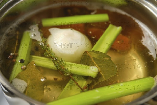 A pot simmers on the stove filled with water, celery stalks, onions, and spices. Fresh herbs like