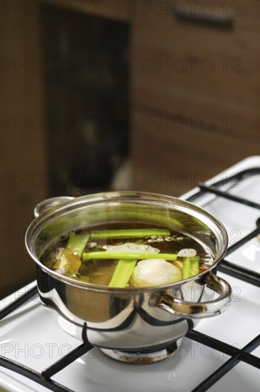 Cooking vegetable broth on the stove in a stainless steel pot with fresh celery, onion, carrot, bay