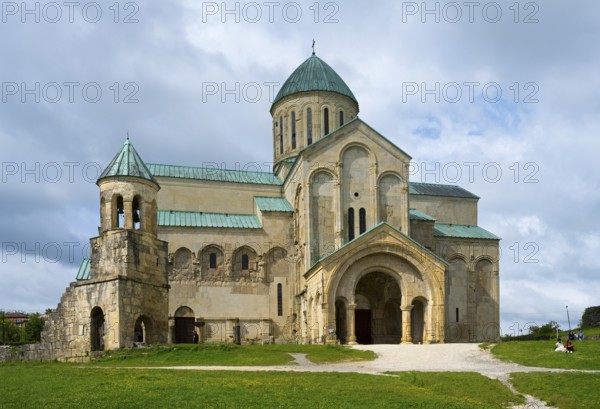 An impressive cathedral with green domes under a cloudy sky in a meadow, Bagrati Cathedral, Church