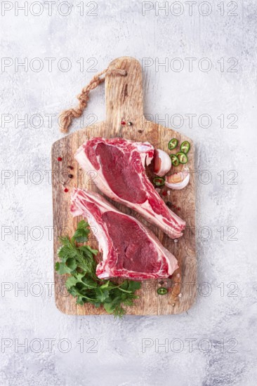 Fresh pieces of beef on the bone, on a wooden cutting board, with herbs and spices, ready for