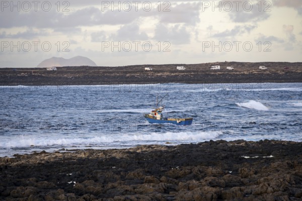 Fishing boat out to sea in the evening, seaside coast with volcanic rocks at sunset, La Santa,