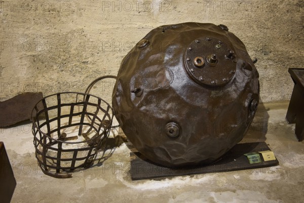 An ancient sea mine next to a metal basket on a concrete floor, War Museum, Military Museum, Tunnel