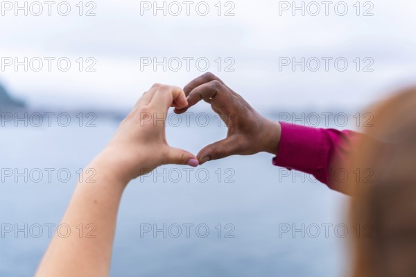 Bride and groom forming a heart shape with their hands against a stunning seascape, celebrating