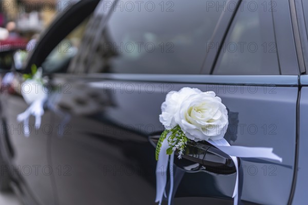 White roses and ribbons elegantly adorn a wedding car door handle, adding a touch of romance and