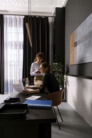 In a contemporary office, two women engage in a productive discussion while reviewing documents.