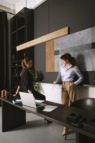 Two women engage in a productive discussion in a sleek office with dark walls and contemporary