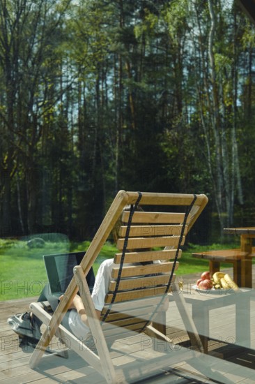 A person enjoys leisure time on a wooden lounge chair, surrounded by picturesque trees and a calm