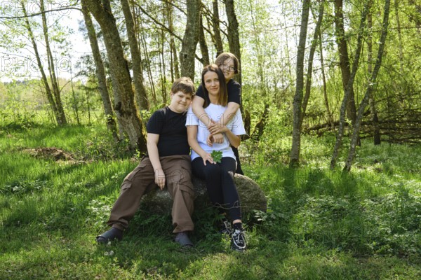 A single mother sits comfortably on a large rock with her two sons in a vibrant green forest