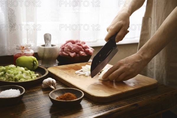 A chef finely chops onion on a wooden cutting board in a warm kitchen. Fresh ingredients like