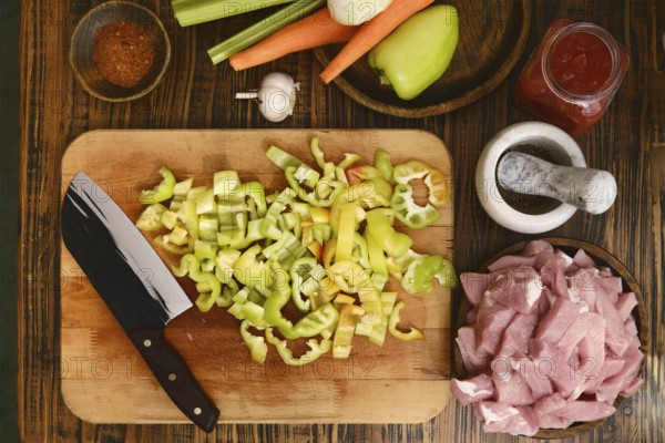 Freshly chopped green bell peppers, celery, and carrots are arranged on a wooden cutting board next