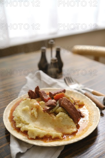 A hearty serving of creamy mashed potatoes topped with tender meat and vegetables on a rustic