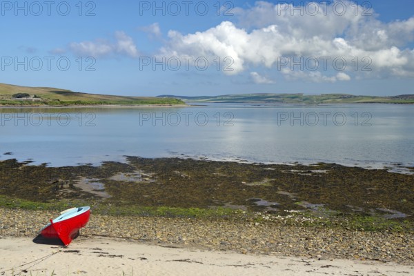 Red boat on the beach with a distant view of the calm sea and a cloudy summer landscape, Hoy,