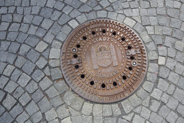 Round manhole cover with town coat of arms, inscription, cobblestones, floor, Ilmenau, Thuringian