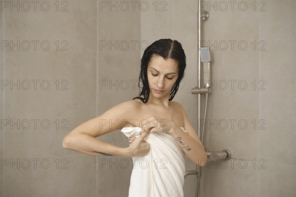 In a modern bathroom, a woman with damp hair adjusts her towel after taking a shower. She appears