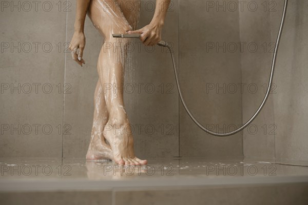 Water cascades over female legs in a sleek bathroom. The individual uses a handheld showerhead to