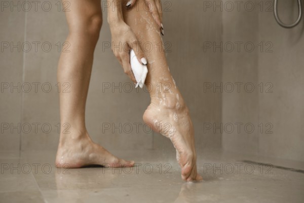 A woman is focused on washing her leg in a bathroom. The soft natural light enhances the clean