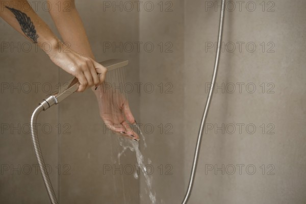 Hands are positioned under flowing water from a sleek showerhead in a stylish bathroom. The setting