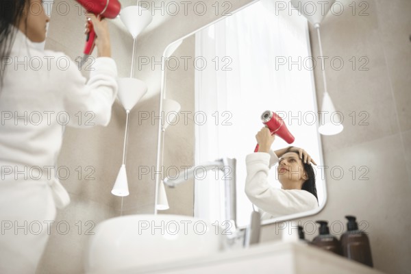 A woman wearing a bathrobe uses a hairdryer while looking in the mirror. The chic bathroom features