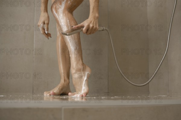 A woman stands in a sleek shower, washing soap off her legs while using a handheld showerhead.